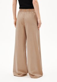 Pantalons large beige en tissu doux, dotés d'une taille élastique et d'une texture lisse, avec une coupe longue et des ourlets nets.