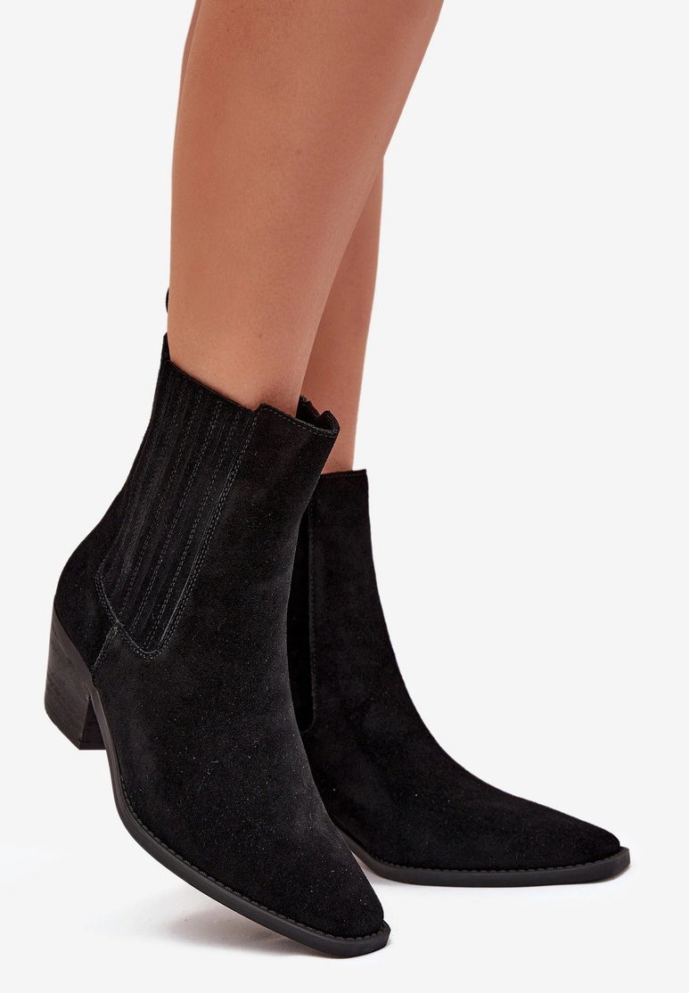 Bottines en suède noir avec un nez pointu, des panneaux latéraux élastiques et un talon empilé. La texture est douce avec une finition mate.