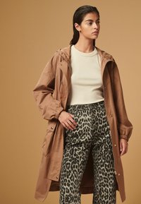 Brūns vieglais jaku ar kapuci, rāvējslēdzēju un elastīgām aprocēm, apvienots ar pelēkam leoparda raksta augsto jostasvietu biksēm un krēmīgu augšu.