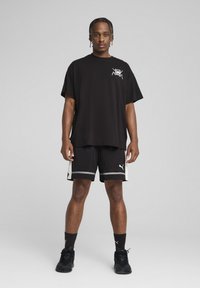 Sort t-shirt med et grafisk logo på venstre bryst, parret med sorte shorts med hvide detaljer og et logo, samt sorte sportssko.