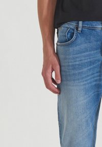 Jeans de mezclilla en lavado azul claro con un diseño de pierna recta, que presentan lazos para cinturón, estilo de cinco bolsillos y un sutil efecto de desgaste.