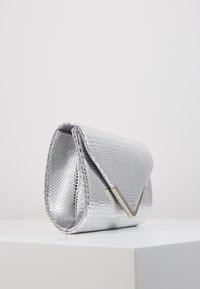 Silverfärgad clutchväska med en strukturerad, ormskinnsliknande mönstring, triangelformad lock och metalliska detaljer. Slät foder inuti. Kompakt form.