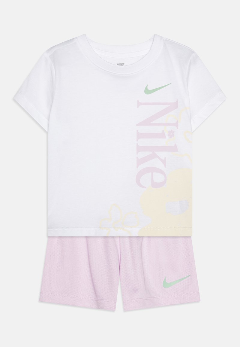 T-shirt branca de algodão com grande impressão rosa "Nike", acentos florais, e calções curtos lavanda com o logótipo verde da Nike.