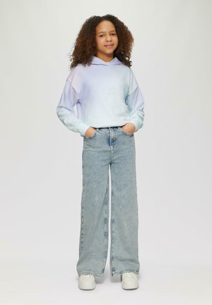 Lichtblauwe gradient hoodie met een kangoeroezak, gecombineerd met lichtblauwe wijde jeans. Model draagt witte sneakers.