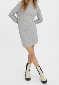 Robe pull en tricot gris avec un motif en zigzag, manches longues et poignets côtelés. Associée à des bottines beiges et noires.