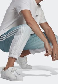 Vit bomullst-shirt med svart Adidas-logotyp, kombinerad med ljusblå och vita joggers med sidostripe och elastiska muddar; vita sneakers.