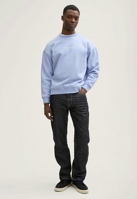 Világoskék pulóver kerek nyakkivágással, laza szabással és hímzett felirattal. Sötét farmerrel és fekete tornacipővel párosítva.