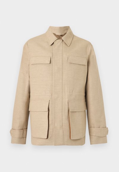 Μπεζ μακρυμάνικο μπουφάν με τέσσερις τσέπες με καπάκι, εμπρόσθιο φερμουάρ κρυμμένο από υφασμάτινη λωρίδα και κλασικό γιακά σε μονόχρωμο φόντο.