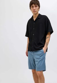 Polo a maniche corte nera, con bottoni e texture a coste, abbinata a pantaloni corti azzurri chiari. L'abbigliamento presenta una vestibilità comoda e un design informale.