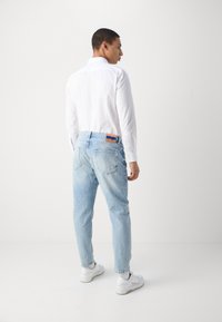 Lys blå, avslappet passform jeans med en slitt tekstur, detaljert med to baklommer og en oransjefarget beltehjul. Kombinert med en hvit skjorte og sneakers.
