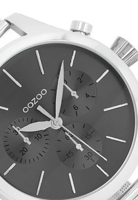 Montre en acier inoxydable ton argent avec un cadran noir, trois sous-cadrans, aiguilles argentées et surface texturée ; présente des marqueurs d'heure minimalistes.