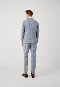 Costum pătat bleu deschis, cu o croială ajustată, având guler cu colț, o deschidere și pantaloni asortați. Pantofi maro completează ținuta.