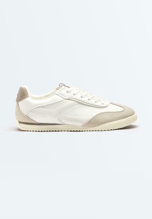 Baskets basses blanches avec détails en daim beige sur les orteils et le talon, lacets blancs et semelle en caoutchouc texturée.