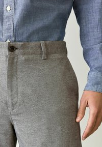 Graue Hosen im Fischgrätenmuster mit Knopfverschluss und seitlichen Taschen, kombiniert mit einem blauen Chambray-Hemd, das texturierte Stoffdetails zeigt.