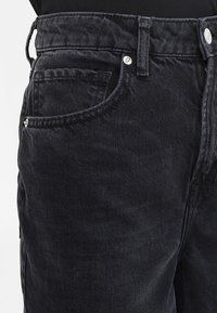 Svarta jeans i denim med en klassisk femficksdesign, stickade detaljer och metallknapp-accessoarer vid midjan och ficköppningarna.