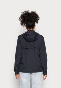 Navy rain jacket with a hood, featuring a zippered back vent and elastic cuffs, paired with light blue denim jeans.