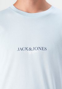 Light blue cotton t-shirt featuring a crew neckline and a navy printed logo "JACK & JONES Originals Studio" on the front.