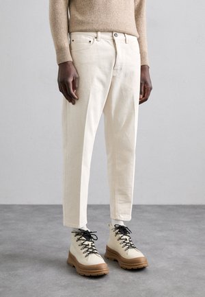 Pantalons en coton de couleur crème avec une coupe décontractée, associés à des bottes de randonnée beiges et brunes avec des lacets noirs et des semelles épaisses.