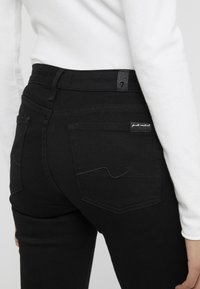 Svarta denimjeans med hög midja, slim fit, med bakfickor och subtila sömmar; etikett synlig på midjebandet.