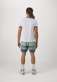 Pánský sportovní outfit s bílou košilí s krátkým rukávem a námořnickými detaily, doplněný kraťasy s vícebarevným gradientem. Bílé sportovní ponožky a boty.