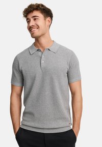 Polo gris de manga corta con un tejido texturizado, tapeta de tres botones y cuello y dobladillo acanalados. Lleva pantalones oscuros.