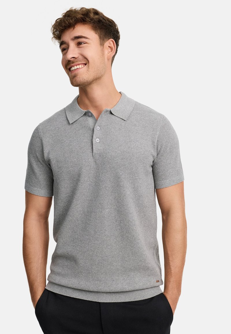 Polo gris de manga corta con un tejido texturizado, tapeta de tres botones y cuello y dobladillo acanalados. Lleva pantalones oscuros.