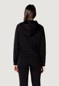 Czarna bluza z kapturem o dopasowanym kroju, z regulowanym kapturem i ściągaczami przy mankietach. Wykonana z miękkiego materiału bawełnianego, pokazana z tyłu.