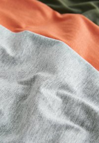 Baumwollstoff mit strukturierter Oberfläche, der drei horizontale Farbsegmente zeigt: Grau, Koralle und Olivgrün.