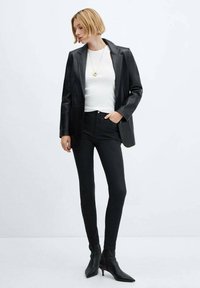 Černý kožený blazer přes bílý top, v kombinaci s černými skinny džíny a špičatými kotníkovými botami. Jednoduchý zlatý náhrdelník jako akcent.
