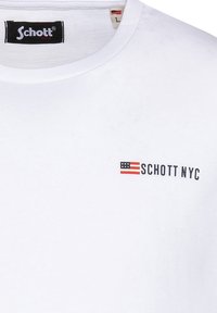 Camiseta de algodón blanca con cuello redondo, un pequeño logo "Schott NYC" en negro y rojo, y un diseño de bandera. Textura suave, ajuste casual.