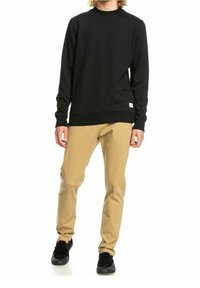 Felpa nera con scollo a girocollo a coste, tessuto elastico; abbinata a pantaloni beige, taglio slim, dalla texture liscia, e sneakers nere.