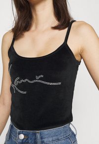 Svart sammetslinne med tunna axelband, prytt med en silver rhinestone-design i ett flytande skript över framsidan. Slät textur.