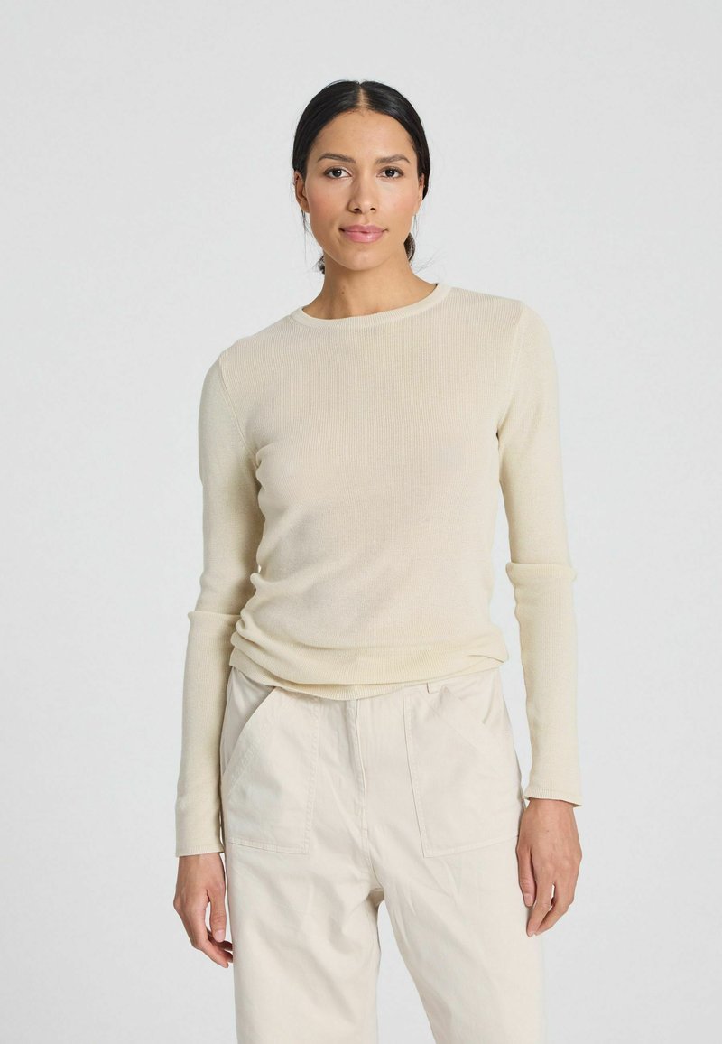 Ribbed long-sleeve top in light beige, featuring a round neckline and fitted silhouette, paired with light beige wide-leg trousers.