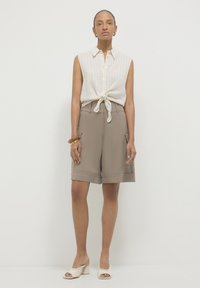 Canotta bianca a righe legata in vita, abbinata a pantaloni corti beige a vita alta con tasche e sandali bianchi con tacco a blocco.