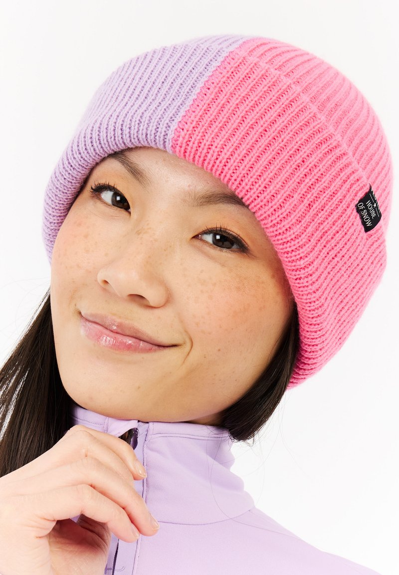 Gebreide beanie met afwisselende secties van roze en lavendel, met een ribbelstructuur en een klein zwart label aan de zijkant.
