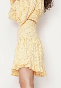 Żółta spódnica w kwiatowy wzór z falbaną u dołu i teksturowanym materiałem. Średniej długości, z dopasowaną talią i miękkim, lekkim materiałem.