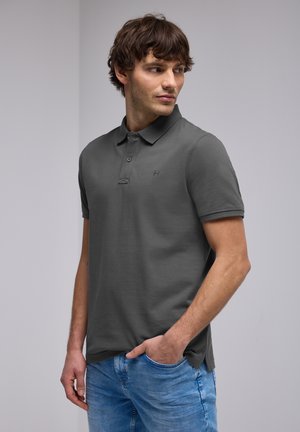 Polo grigio con maniche corte, texture liscia, patta con due bottoni e logo sottile. Abbinato a jeans azzurri chiari.