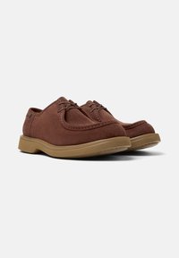 Scarpe in suede marrone con suola in gomma spessa e lacci, posizionate in modo prominente su uno sfondo bianco semplice.