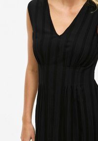 Abito nero con scollo a V, design senza maniche e texture a righe verticali, con corpino aderente e gonna svasata.