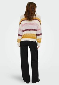 Strickpullover mit mehrfarbigen Streifen in Creme, Gelb, Pink und Burgunderrot. Oversized-Schnitt, gerippte Bündchen und Saum. Kombiniert mit schwarzen weit geschnittenen Hosen.