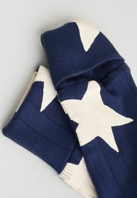 Chaussettes tricotées bleues et blanches avec de grands motifs d'étoiles blanches pliées sur une surface gris clair.