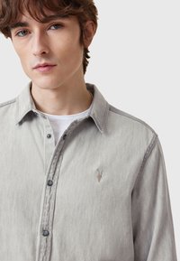 Hellgraues Jeanshemd mit langen Ärmeln, Knopfleiste und dunklen Knöpfen. Verfügt über ein dezentes, gesticktes Logo auf der Brust.