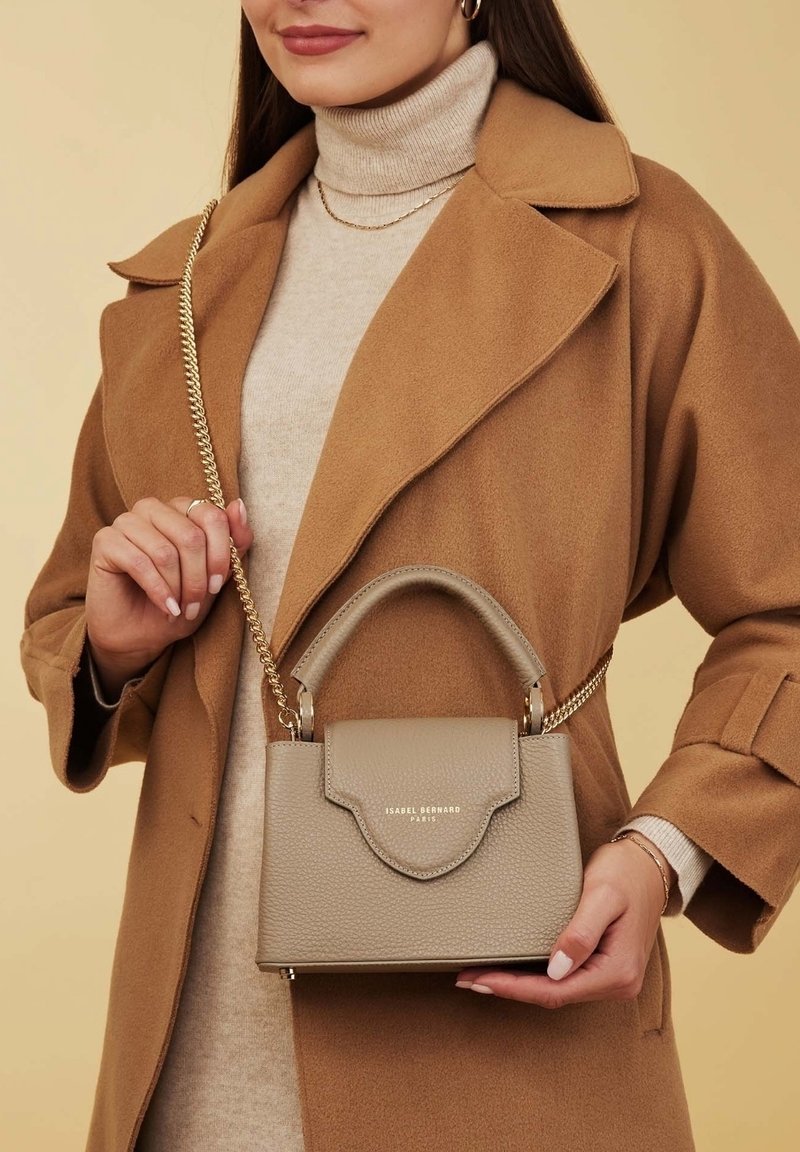 Sac à main en cuir gris avec un design structuré, une poignée supérieure et une bandoulière en chaîne. Il possède une fermeture à rabat et le nom de la marque embossé en or.