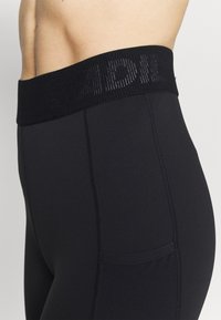 Leggings de sport noirs avec une ceinture large texturée. Comprend une poche latérale et des détails cousus le long des jambes.