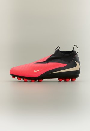Κόκκινο και μαύρο ποδοσφαιρικό παπούτσι Nike με μπεζ σήμα swoosh, μορφοποιημένες τάπες, θηλιές στη φτέρνα και στη γλώσσα, σε πλευρική άποψη πάνω σε ουδέτερο φόντο.
