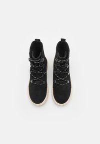 Sorte semskede høyhælte støvler med kontrasterende off-white gummisåler, som har metallisk snørehardware og en polstret krage. Tekstuert snører inkludert.
