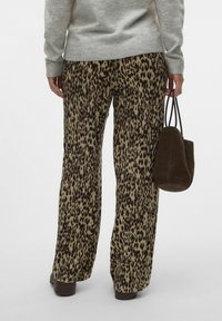 Hlače s širokim nogavicama u leopard printu u bež i tamno smeđoj boji, uparene sa sivim džemperom i smešnim suknjicama od kože, pokazuju ležeran kroj.