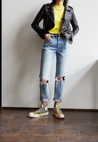 Svart läderbikerjacka, gul T-shirt, rivna ljusblå jeans och högsneakers med leopardmönster, accentuerat med nätstrumpor.