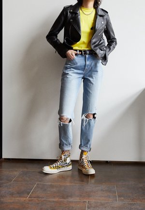 Svart läderbikerjacka, gul T-shirt, rivna ljusblå jeans och högsneakers med leopardmönster, accentuerat med nätstrumpor.