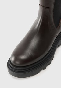 Stivale alla caviglia in pelle marrone con punta arrotondata, pannelli elastici laterali e suola in gomma nera spessa con superficie texture.
